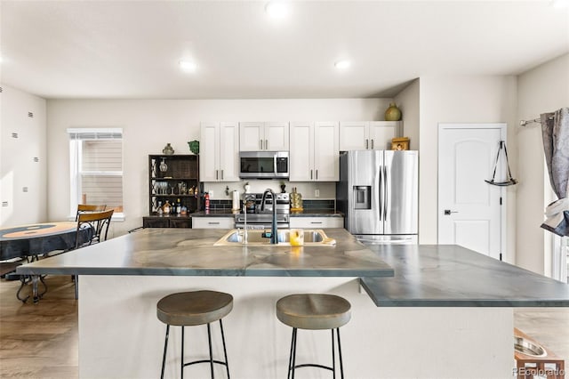 kitchen featuring a kitchen bar, dark countertops, a kitchen island with sink, and stainless steel appliances