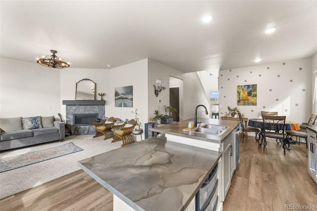 kitchen with an island with sink, a glass covered fireplace, light wood-type flooring, and a sink