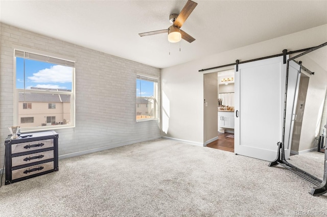 carpeted bedroom featuring baseboards, brick wall, ceiling fan, a barn door, and connected bathroom