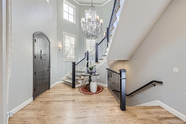 entryway featuring crown molding, light hardwood / wood-style flooring, a chandelier, and a high ceiling