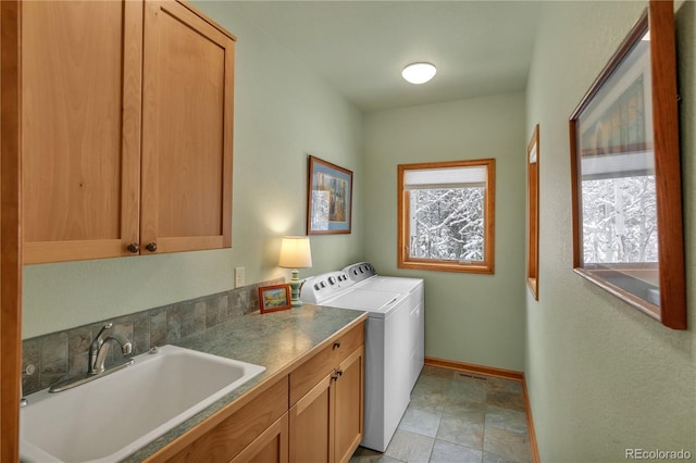 washroom featuring baseboards, stone finish floor, washer and clothes dryer, a sink, and cabinet space