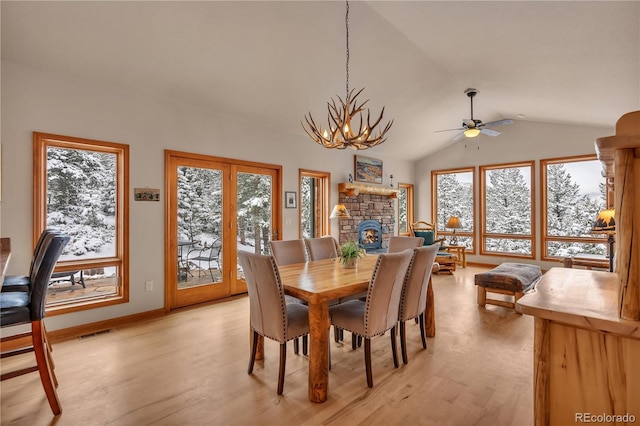 dining space with a stone fireplace, ceiling fan with notable chandelier, vaulted ceiling, light wood-type flooring, and visible vents
