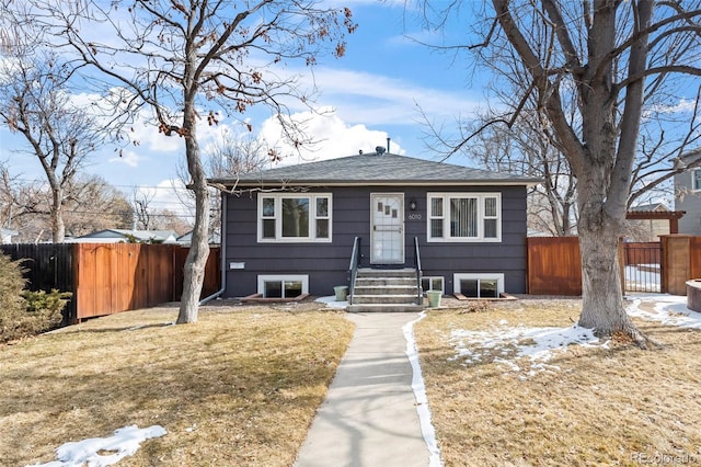 bungalow-style home with a shingled roof, fence, and a front yard