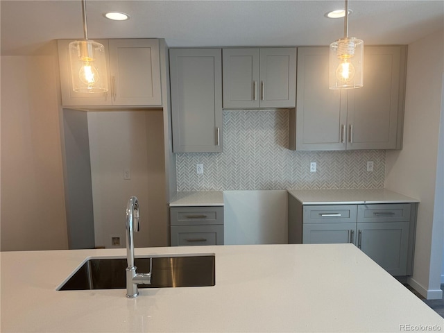 kitchen featuring light countertops, decorative backsplash, a sink, and gray cabinetry