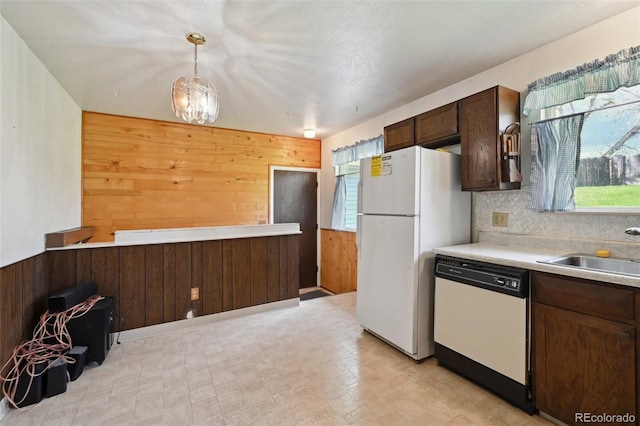 kitchen with dark brown cabinets, a sink, white appliances, light countertops, and wood walls