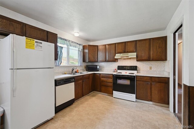 kitchen with white appliances, light countertops, under cabinet range hood, tasteful backsplash, and a sink