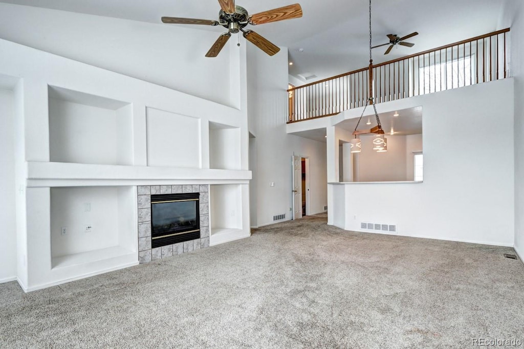 unfurnished living room featuring a tile fireplace, carpet, a towering ceiling, and ceiling fan