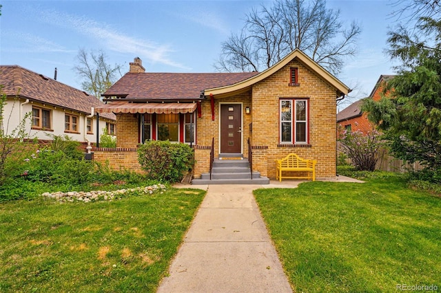 bungalow-style house with fence, roof with shingles, brick siding, a front yard, and a chimney