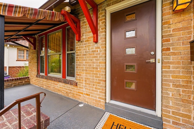 view of exterior entry featuring covered porch and brick siding