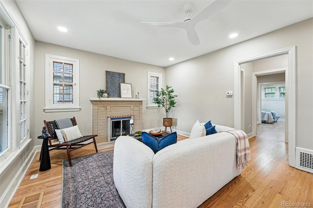 living area featuring a fireplace, a ceiling fan, visible vents, and light wood-style floors