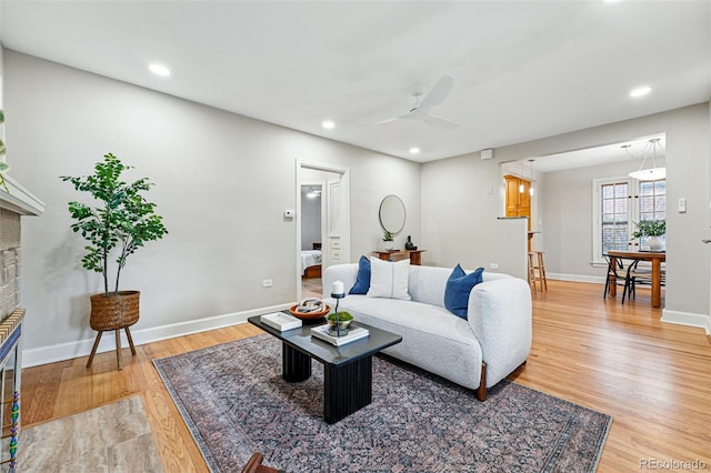living room featuring ceiling fan, light wood finished floors, a brick fireplace, recessed lighting, and baseboards
