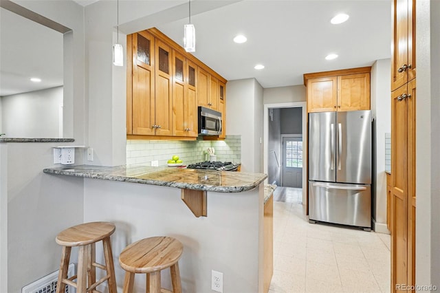 kitchen featuring decorative backsplash, a peninsula, light stone countertops, a kitchen bar, and stainless steel appliances