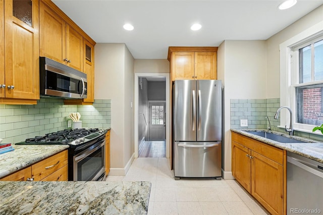 kitchen with a sink, brown cabinets, light stone countertops, and stainless steel appliances