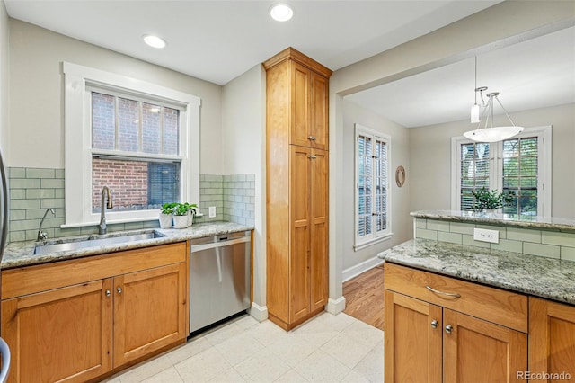 kitchen with brown cabinets, light stone counters, a sink, dishwasher, and decorative backsplash