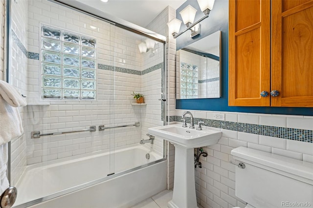 bathroom featuring enclosed tub / shower combo, a healthy amount of sunlight, toilet, and tile walls