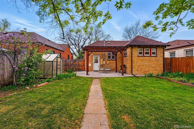 back of property featuring a lawn, a greenhouse, brick siding, a fenced backyard, and a patio