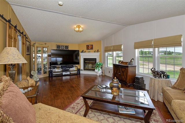 living room featuring a barn door, dark hardwood / wood-style floors, a textured ceiling, and vaulted ceiling