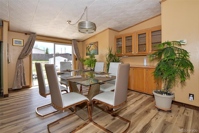 dining space with light wood-type flooring, crown molding, and vaulted ceiling