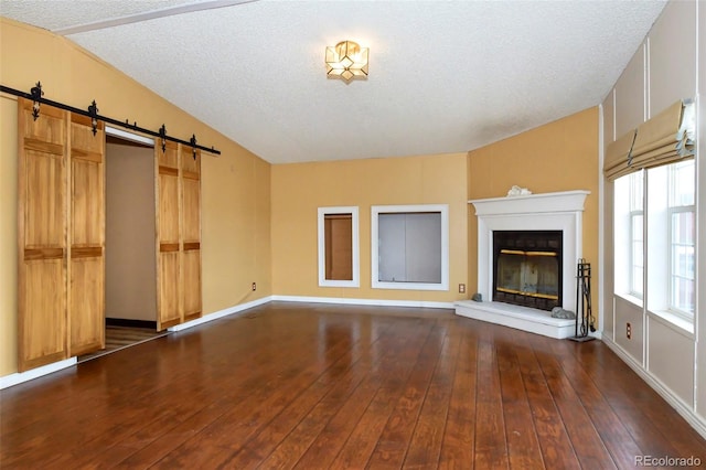 unfurnished living room with a barn door, dark hardwood / wood-style flooring, and a textured ceiling