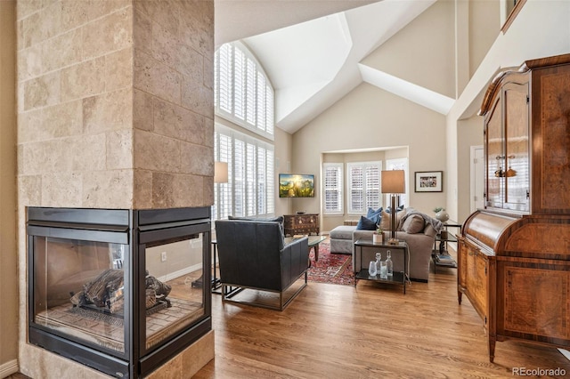 living room with high vaulted ceiling, a tiled fireplace, and wood finished floors