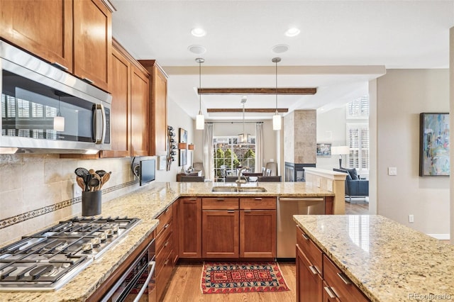 kitchen with a peninsula, a sink, appliances with stainless steel finishes, light wood finished floors, and brown cabinetry