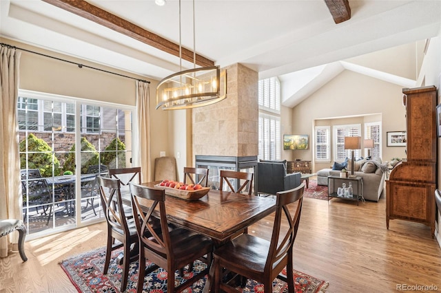 dining area featuring a tile fireplace, vaulted ceiling with beams, an inviting chandelier, and wood finished floors