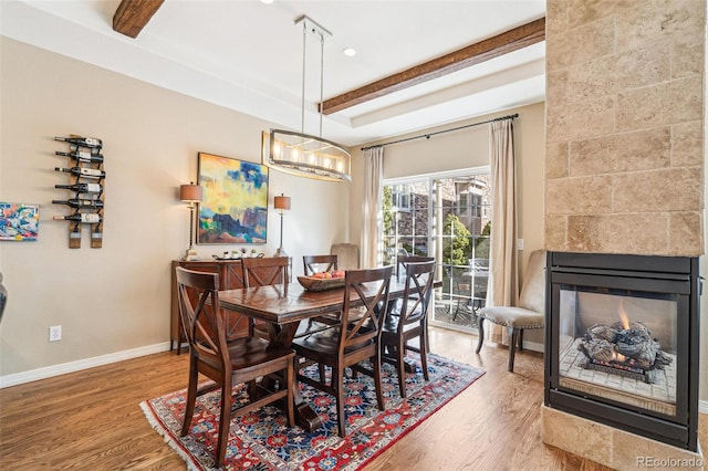 dining area featuring a multi sided fireplace, wood finished floors, beam ceiling, and baseboards