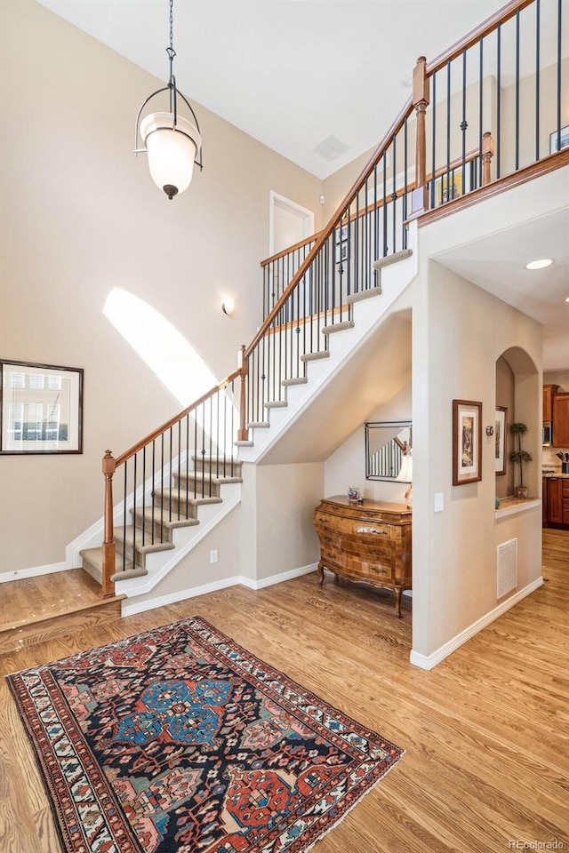 staircase featuring baseboards, visible vents, arched walkways, wood finished floors, and a high ceiling