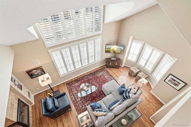 living area with high vaulted ceiling, visible vents, baseboards, and wood finished floors