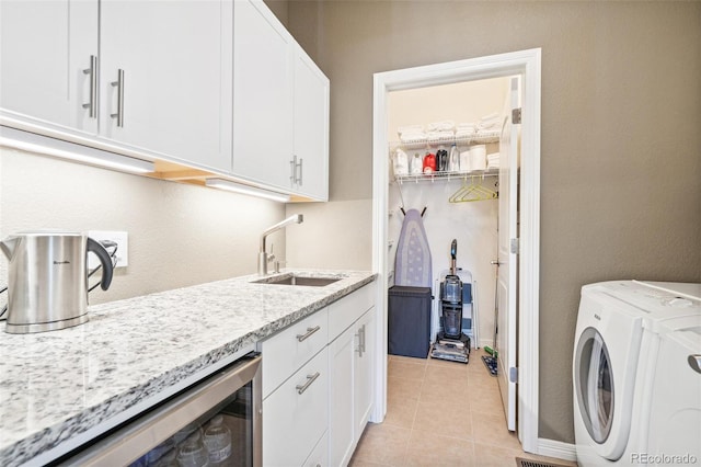 clothes washing area featuring light tile patterned floors, cabinet space, a sink, washer / dryer, and beverage cooler