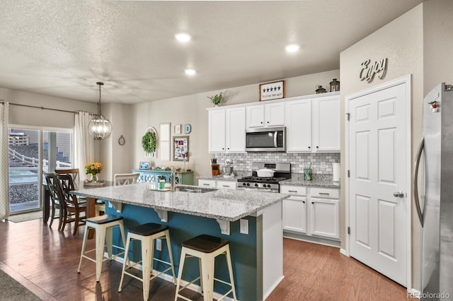 kitchen featuring wood finished floors, a sink, white cabinets, appliances with stainless steel finishes, and backsplash