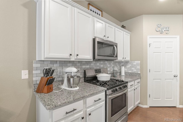 kitchen featuring light wood-style flooring, tasteful backsplash, white cabinetry, appliances with stainless steel finishes, and light stone countertops