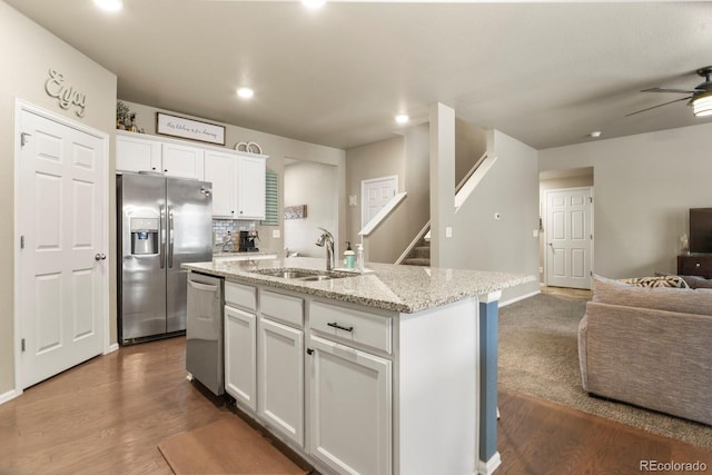 kitchen with an island with sink, a sink, open floor plan, white cabinetry, and appliances with stainless steel finishes