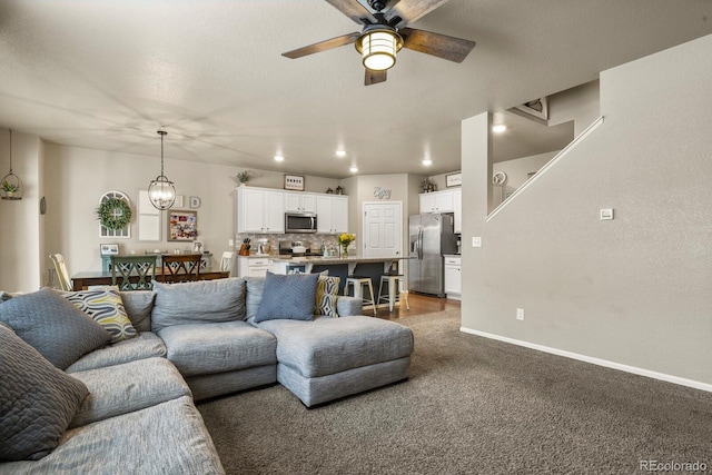 living area featuring recessed lighting, ceiling fan with notable chandelier, baseboards, and dark colored carpet