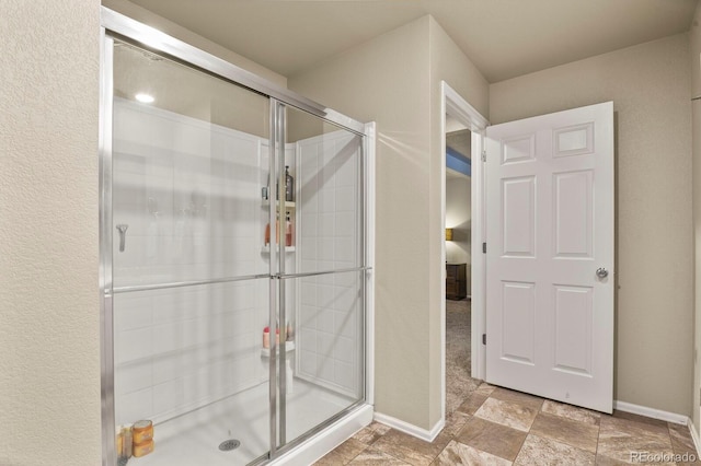 bathroom with baseboards, a stall shower, and stone finish flooring