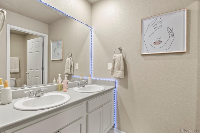 bathroom with double vanity, toilet, a textured wall, and a sink