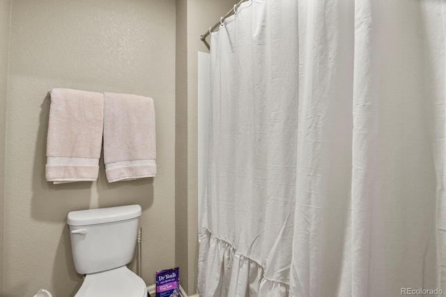 full bath with a shower with shower curtain, toilet, and a textured wall