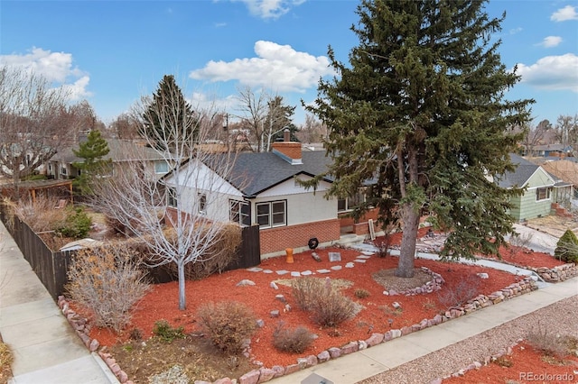 ranch-style home with a shingled roof, brick siding, a chimney, and stucco siding