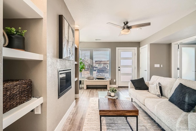 living room with a tiled fireplace, light hardwood / wood-style flooring, and ceiling fan