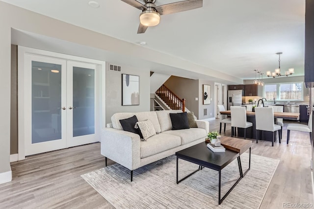 living room with light hardwood / wood-style floors, ceiling fan with notable chandelier, and french doors