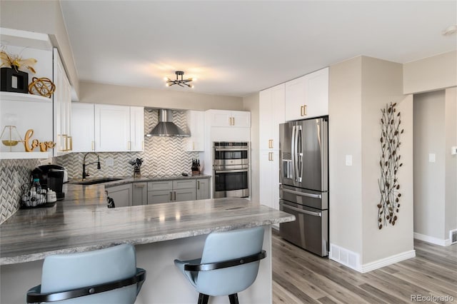 kitchen with a kitchen bar, sink, appliances with stainless steel finishes, kitchen peninsula, and wall chimney range hood