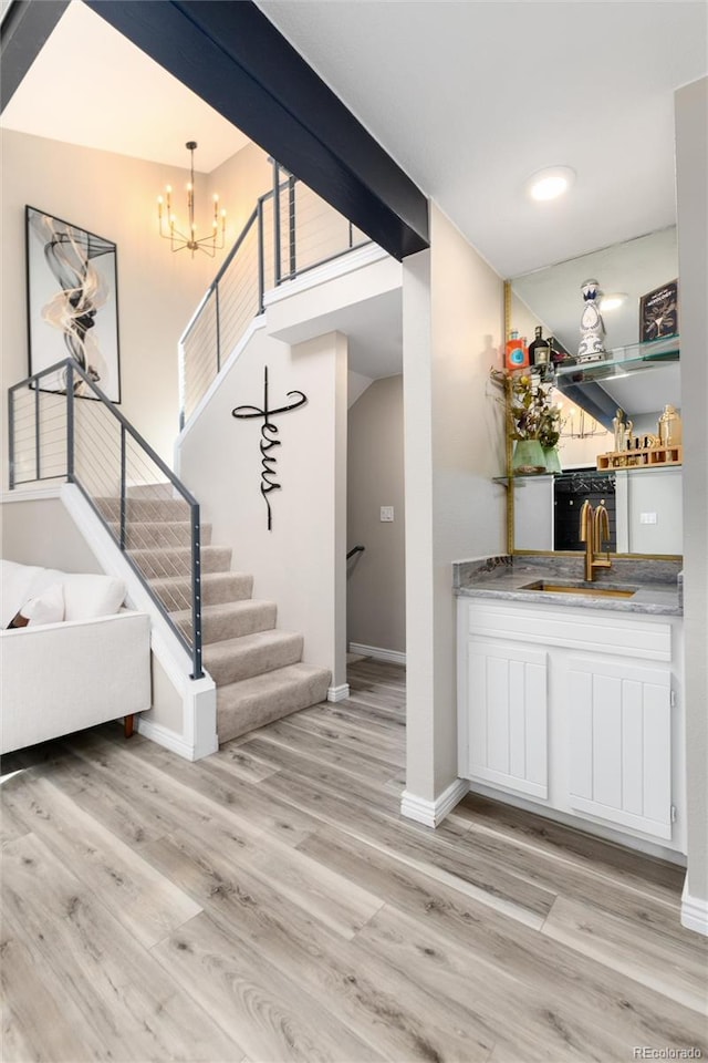 interior space featuring decorative light fixtures, sink, light wood-type flooring, white cabinets, and an inviting chandelier