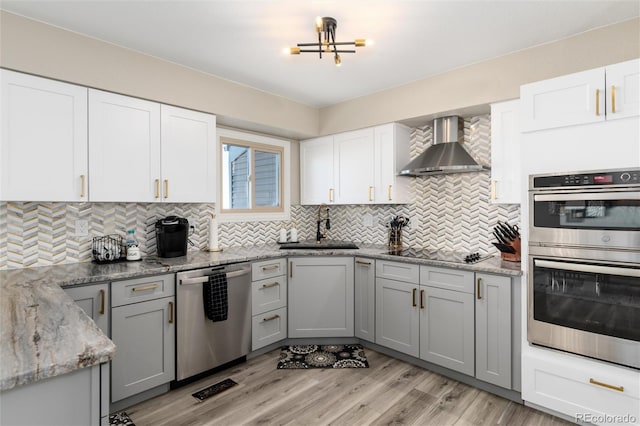 kitchen with sink, gray cabinetry, stainless steel appliances, light stone countertops, and wall chimney exhaust hood