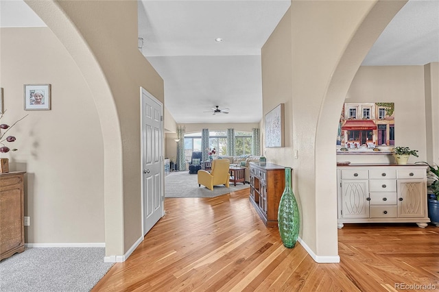 corridor with baseboards, arched walkways, and light wood-type flooring