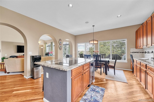 kitchen with a kitchen island, black electric cooktop, light stone counters, light wood finished floors, and wine cooler