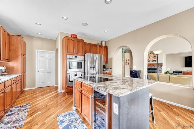 kitchen featuring wine cooler, appliances with stainless steel finishes, arched walkways, and light stone counters