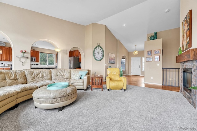 carpeted living area with baseboards, arched walkways, a glass covered fireplace, and high vaulted ceiling