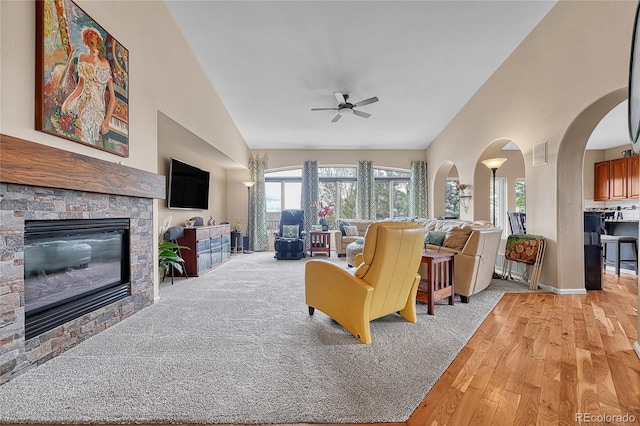 living room with a fireplace, light wood-style floors, baseboards, arched walkways, and a ceiling fan