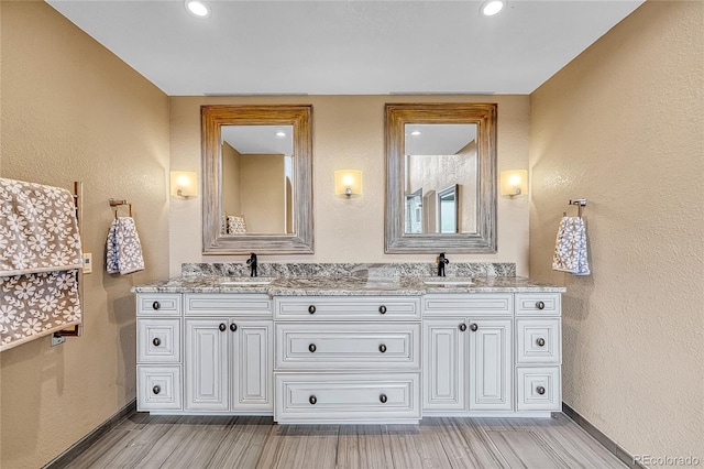 full bath featuring double vanity, baseboards, a sink, and wood finished floors