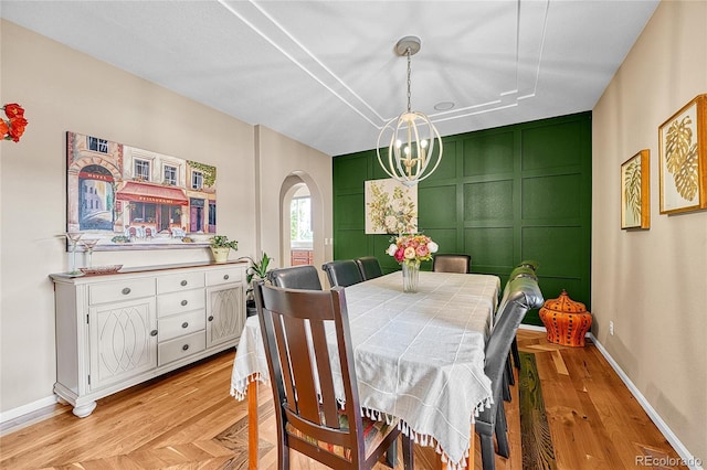 dining area featuring a decorative wall, arched walkways, a chandelier, baseboards, and light wood-type flooring